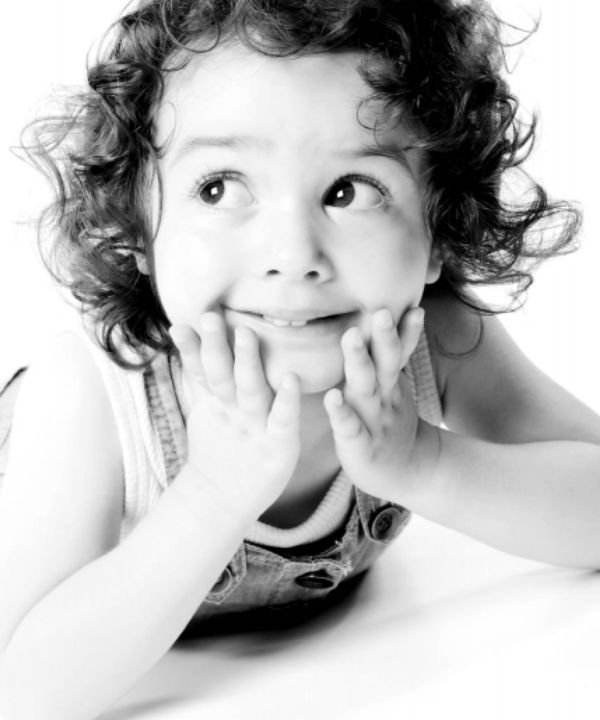 Black and white studio portrait of a young girl with curly hair resting her chin on her hands