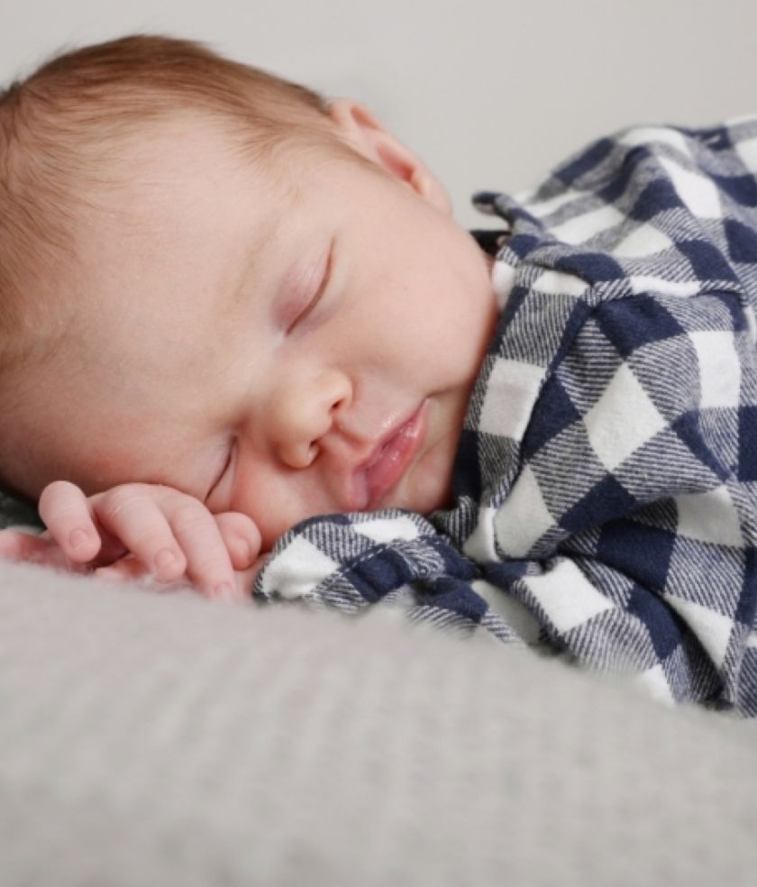 A newborn asleep in a checked shirt on a soft grey blanket