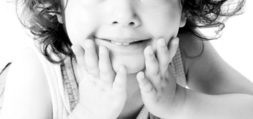 Black and white studio portrait of a young girl with curly hair resting her chin on her hands