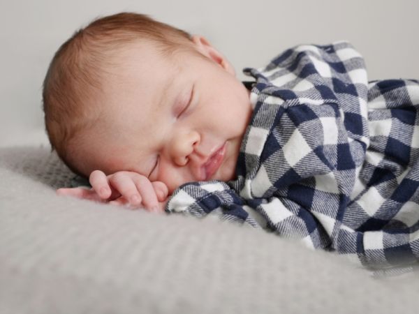 A newborn asleep in a checked shirt on a soft grey blanket