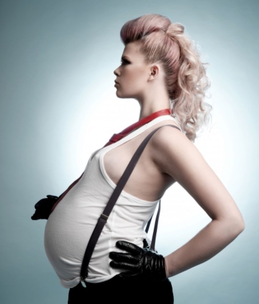 Studio maternity portrait in profile, an expectant mother in braces and a vest against a soft teal background